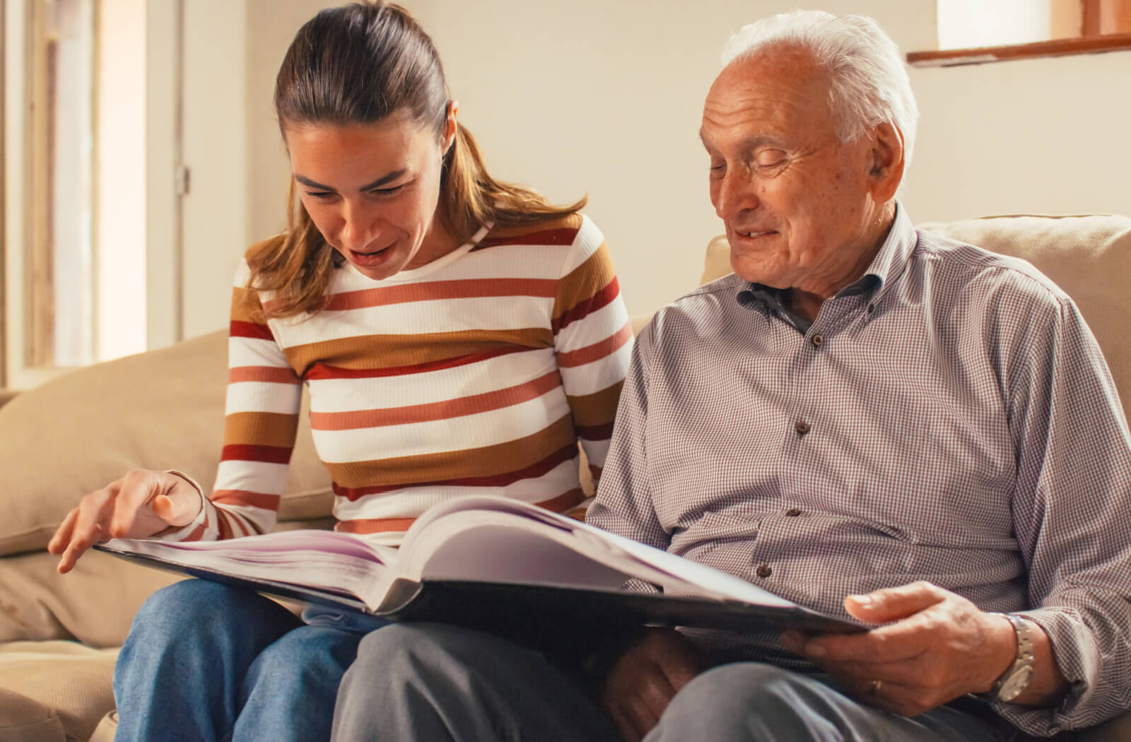 A senior man and his daughter smiling while looking at a photo album together.
