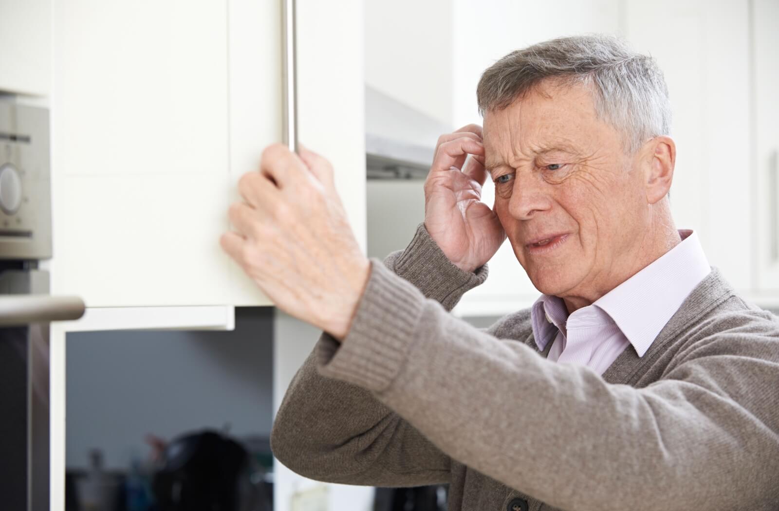 An older adult man with a forgetful look staring at a cupboard trying to remember something.