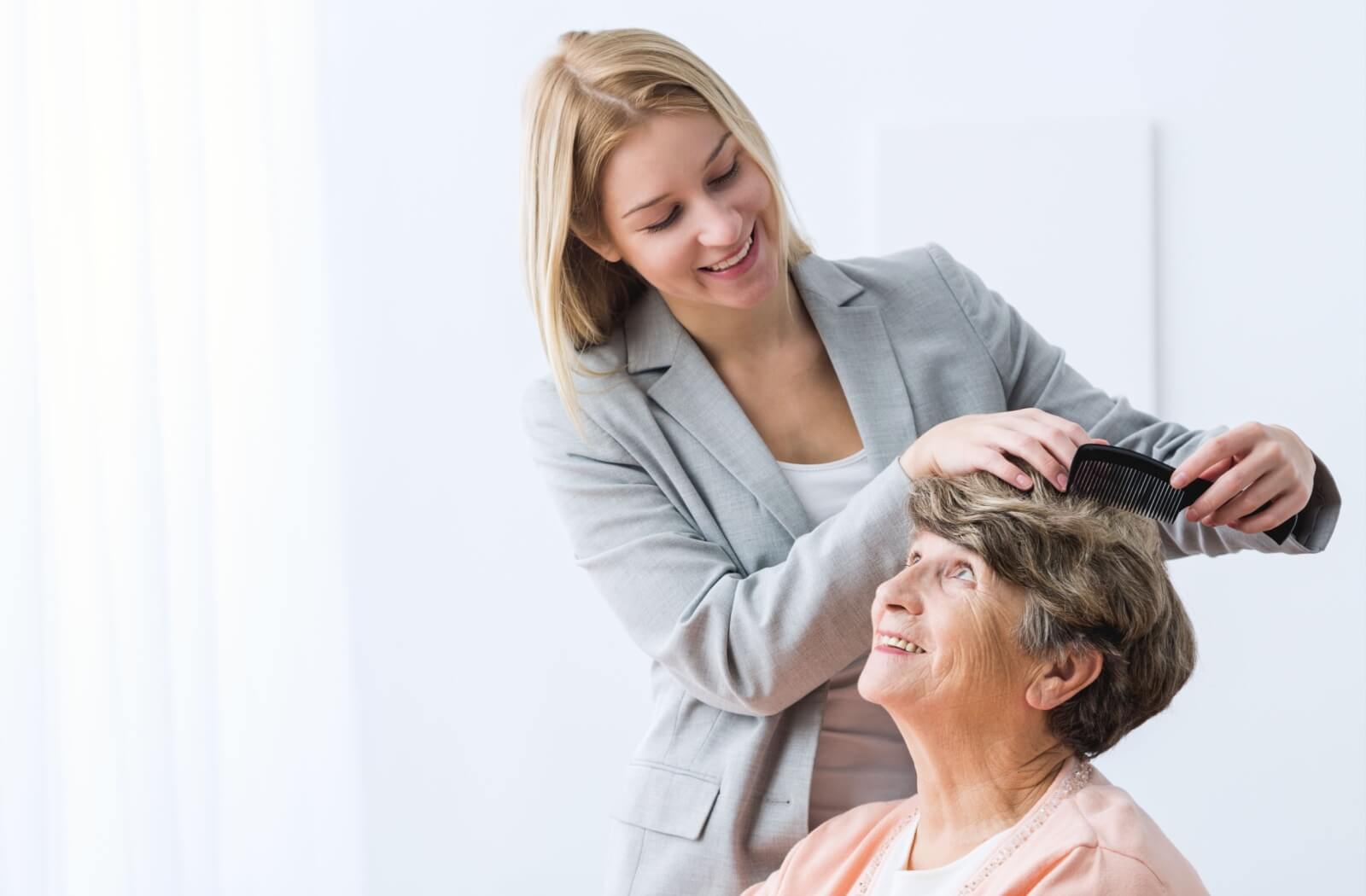 A professional-looking woman combing the hair of her older adult mother.