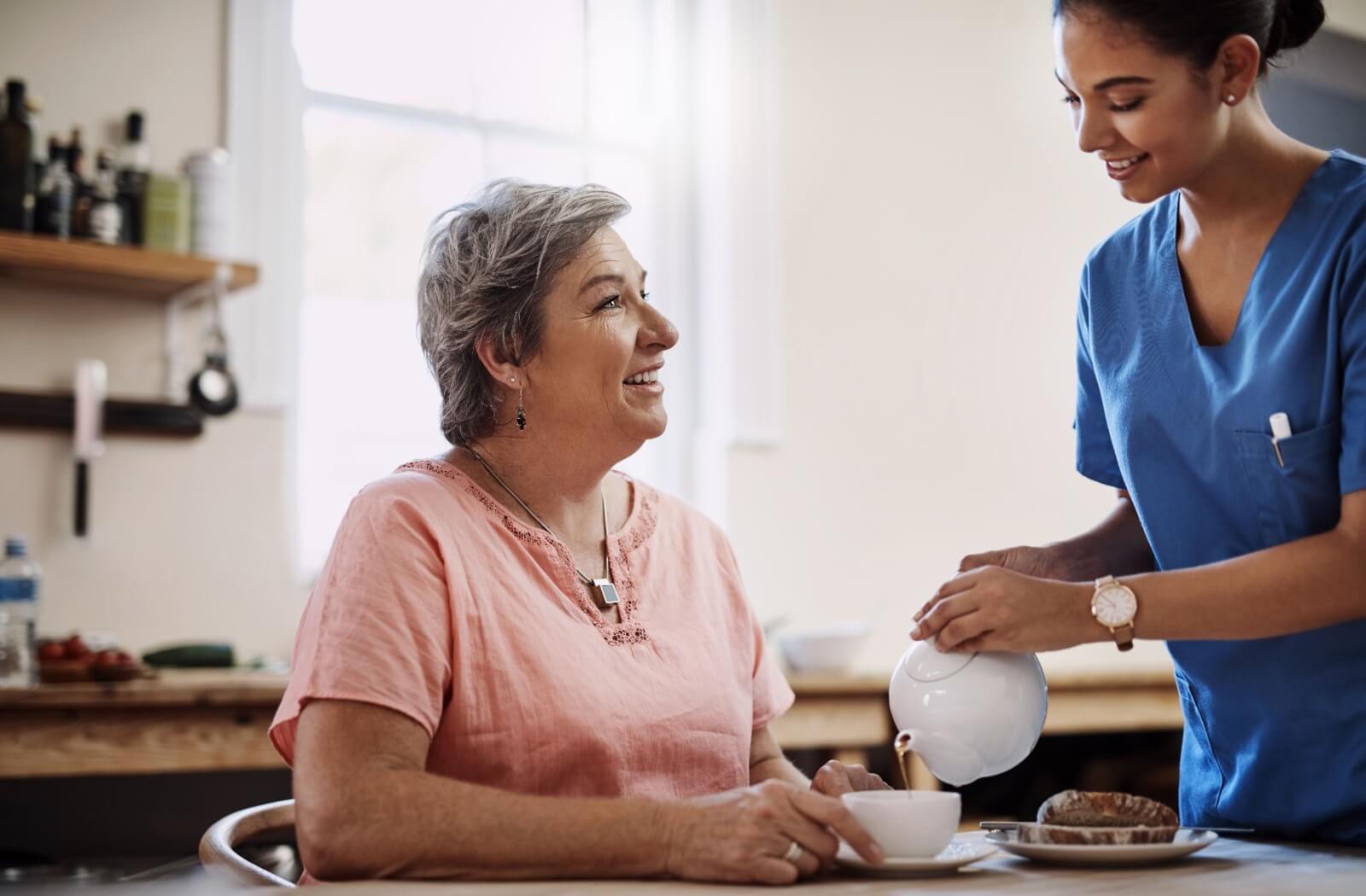 A staff member of a memory care community serving tea to a resident.