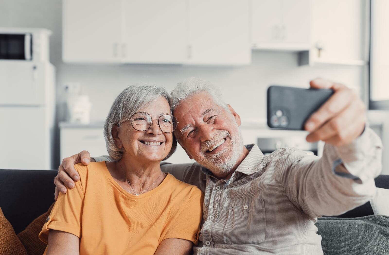 A happy older adult couple using a smart phone to take a selfie.