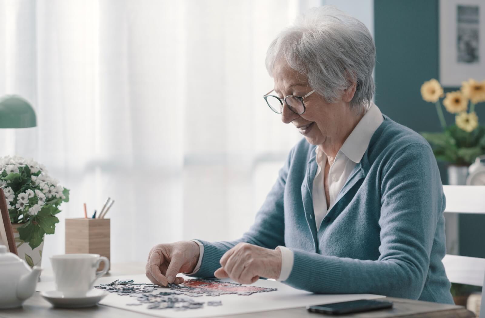 A happy older adult woman solving a jigsaw puzzle.