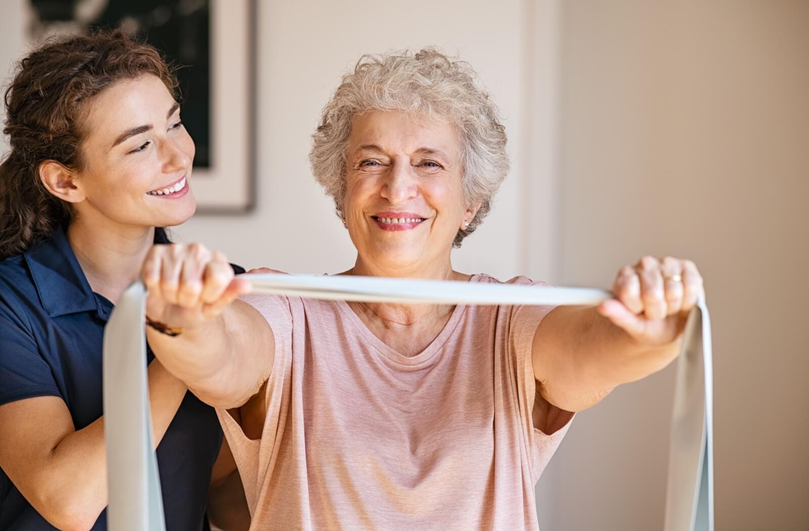 A personal care staff coaching an older adult woman while she exercises.