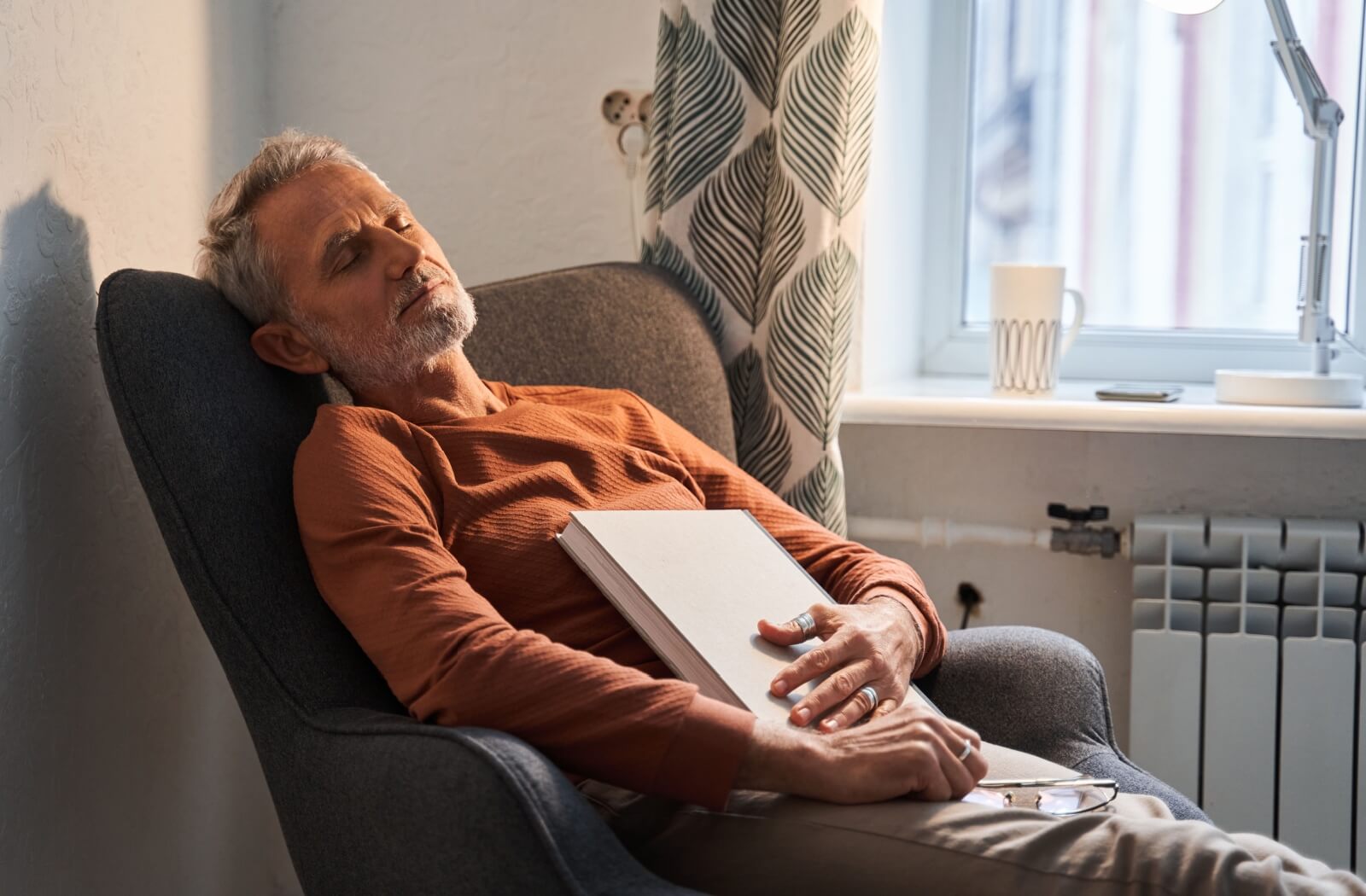 An older adult who fell asleep with a book on his lap.