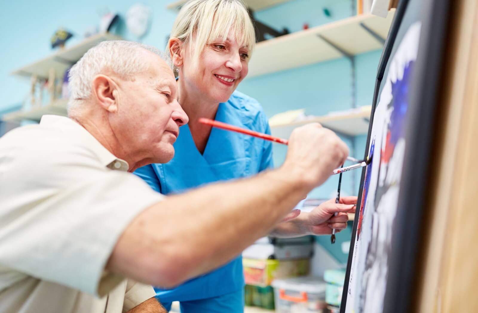 An older adult man painting a picture as part of an art therapy program.