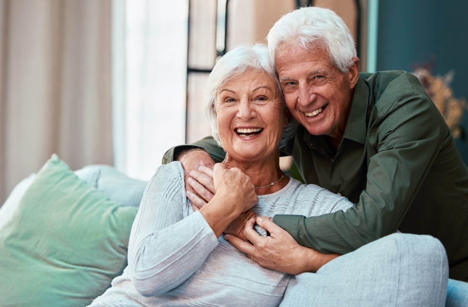 An older adult couple hugging and smiling on a couch.