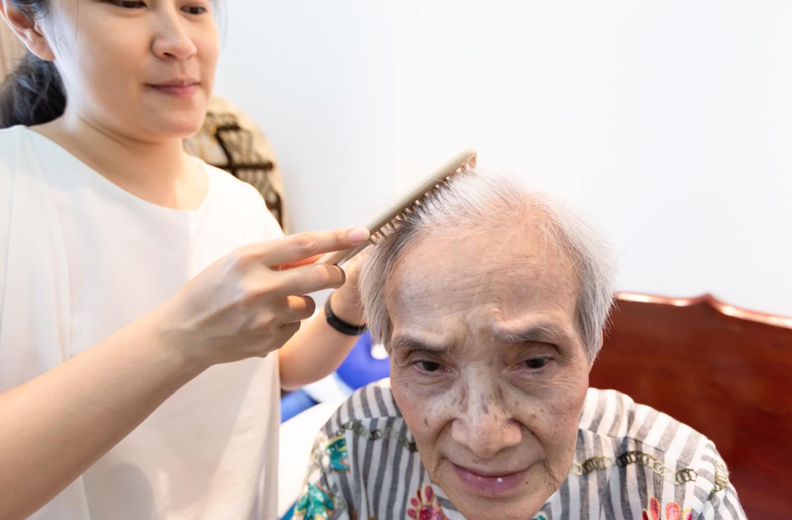 A young care assistant gently combing the hair of an elderly woman as part of daily grooming activities in the personal care home.