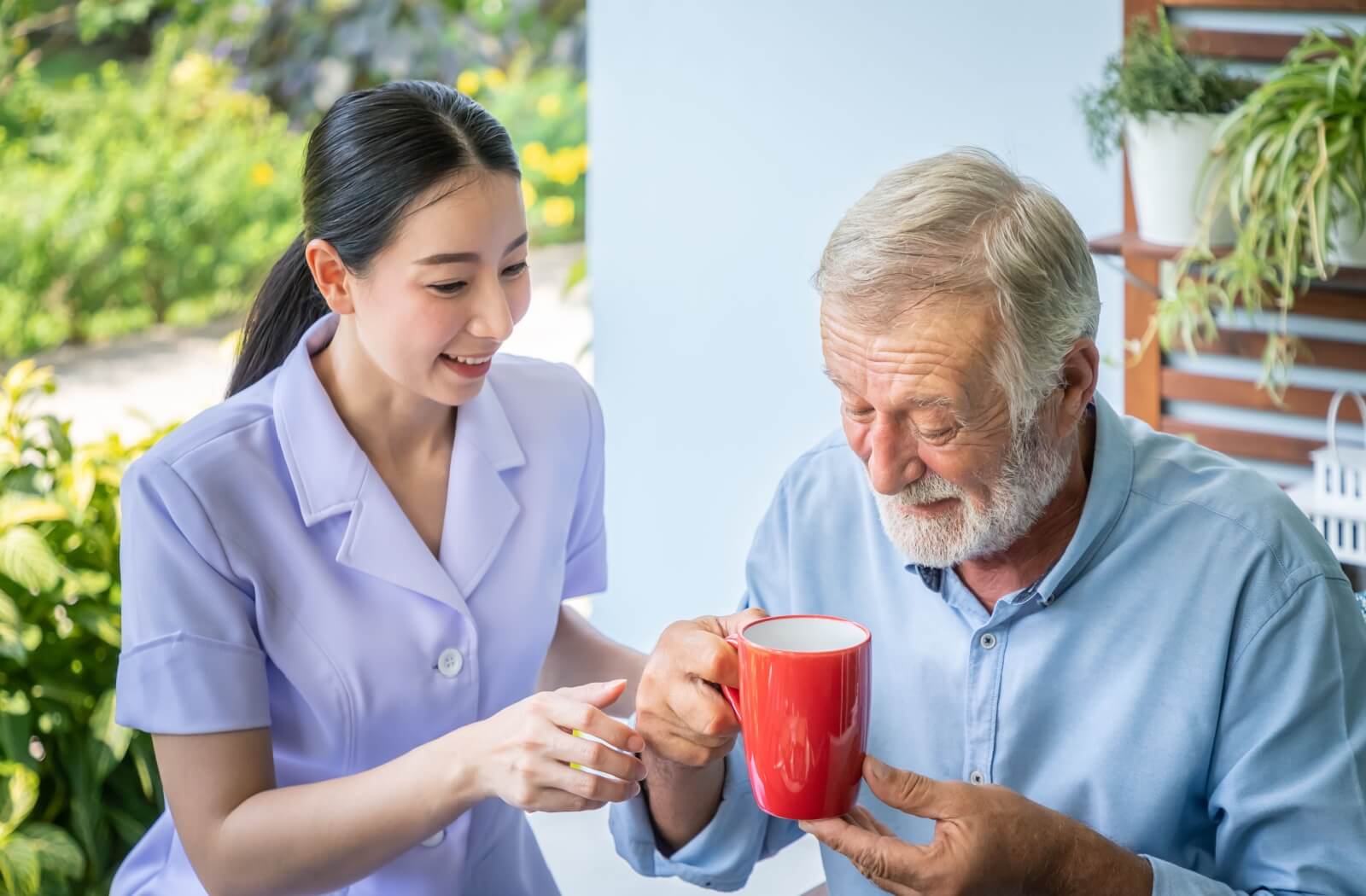 A care assistant offering a coffee cup to an elderly resident during daily activities in the personal care home.