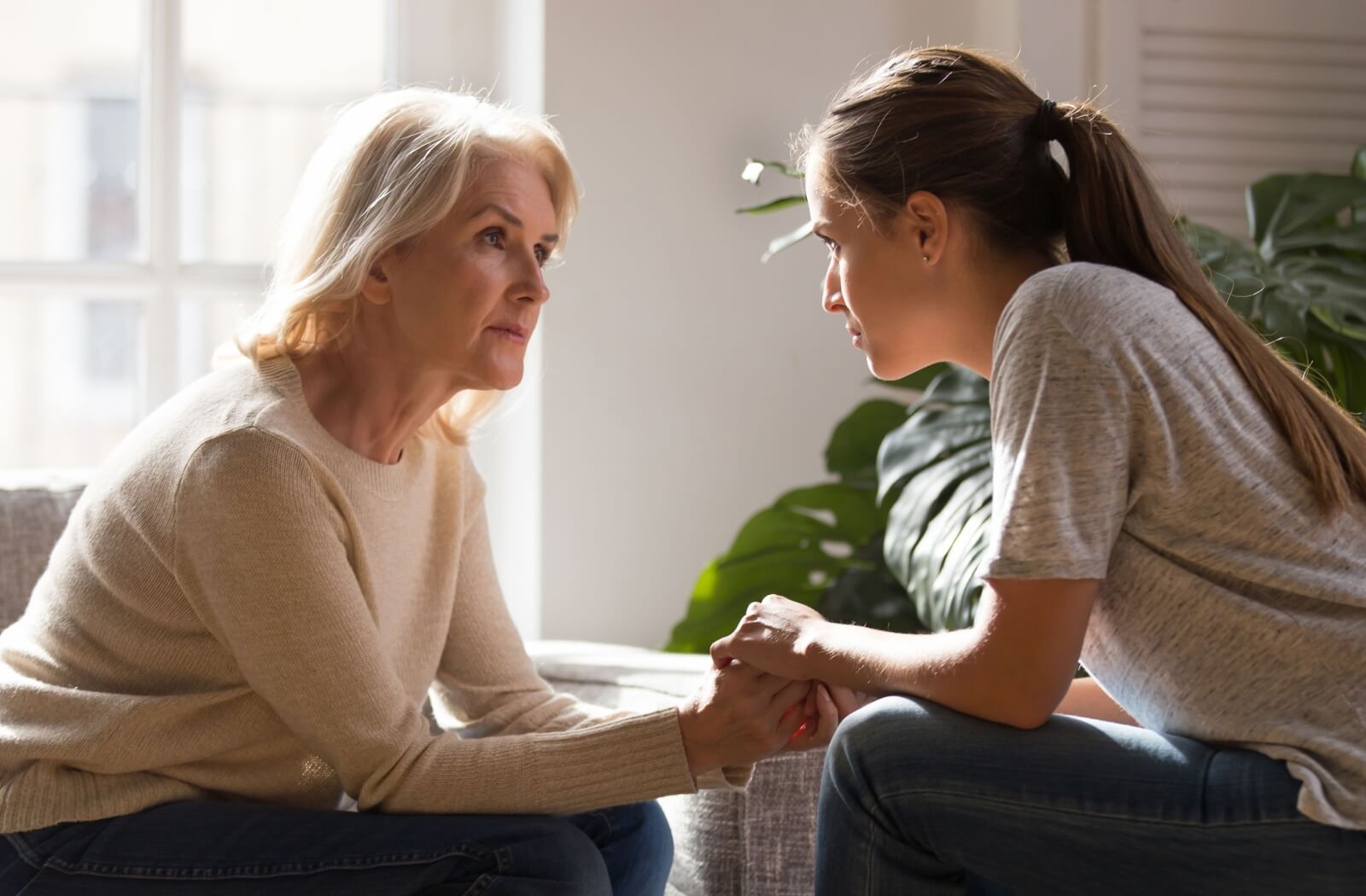 A grown daughter holding hands with her middle-aged mother, sitting together in the assisted living community during a heartfelt conversation about possibly leaving