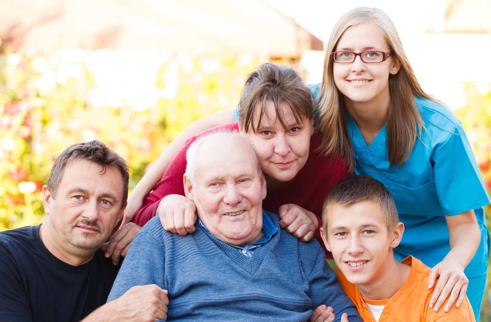 An older adult man, his family, and a caring nurse gather together.