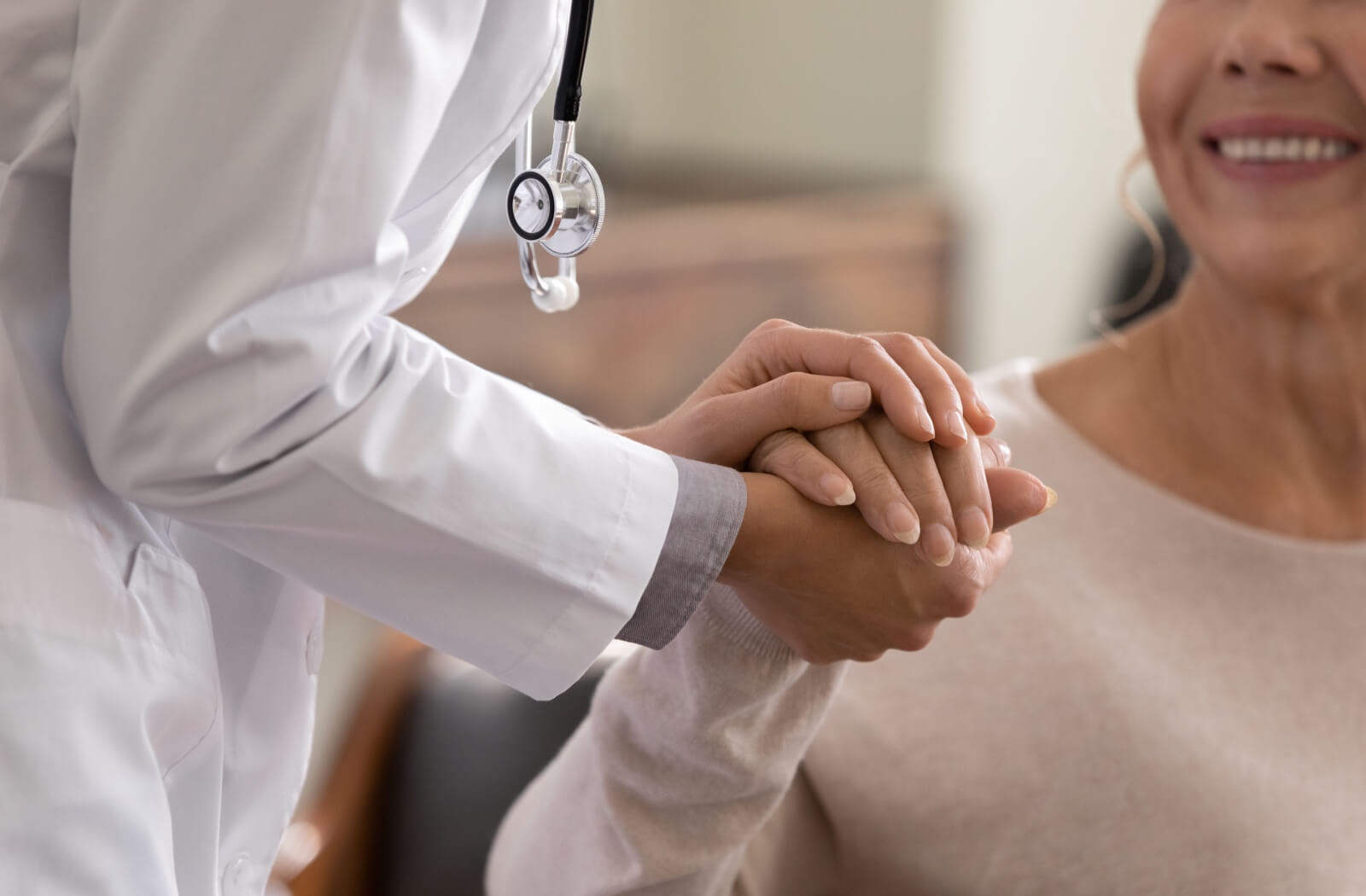 A physician holds the hand of a smiling older adult during a checkup.