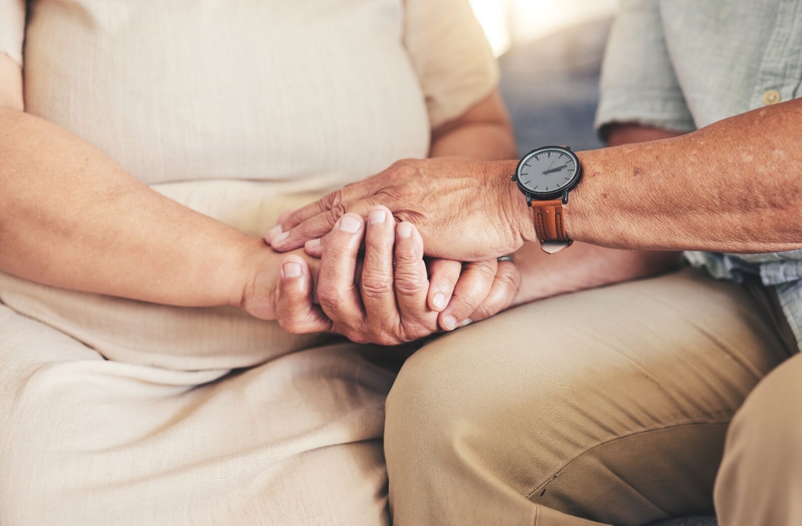 An older adult husband and wife grip each other's hand.