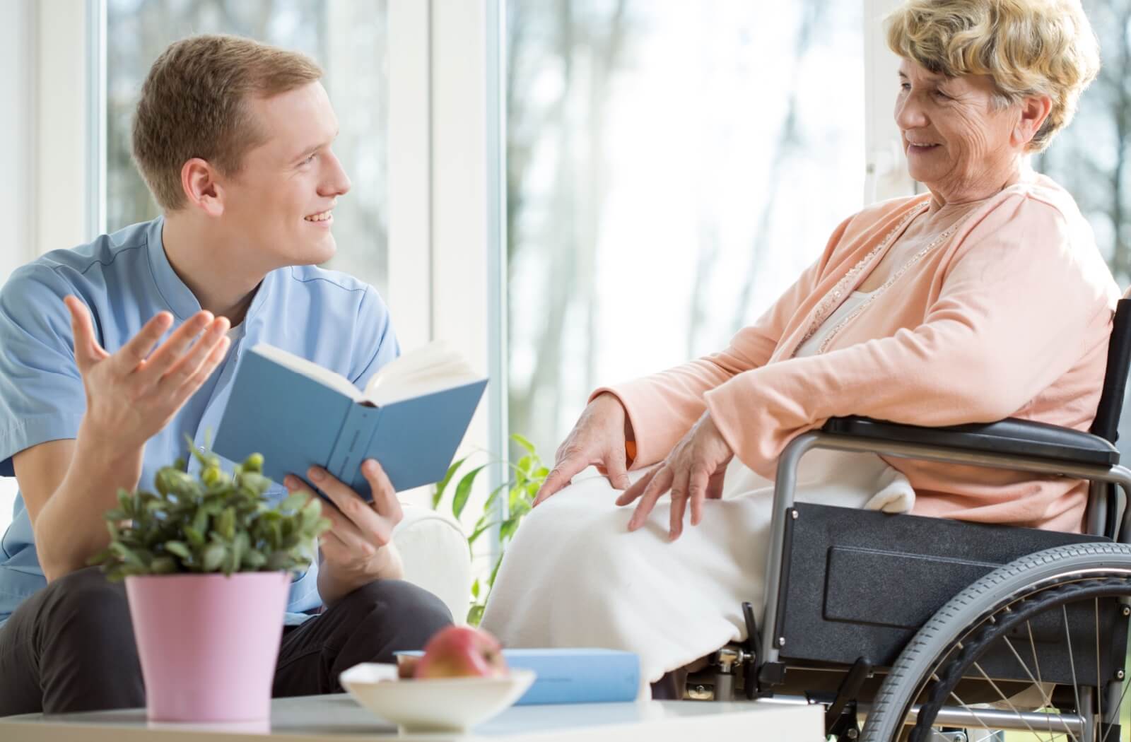 A male care assistant reading a book about Alzheimer's to a senior woman