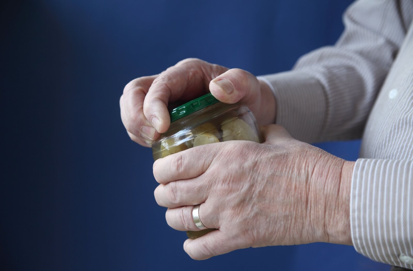 An older adult struggles to open a jar of pickles.
