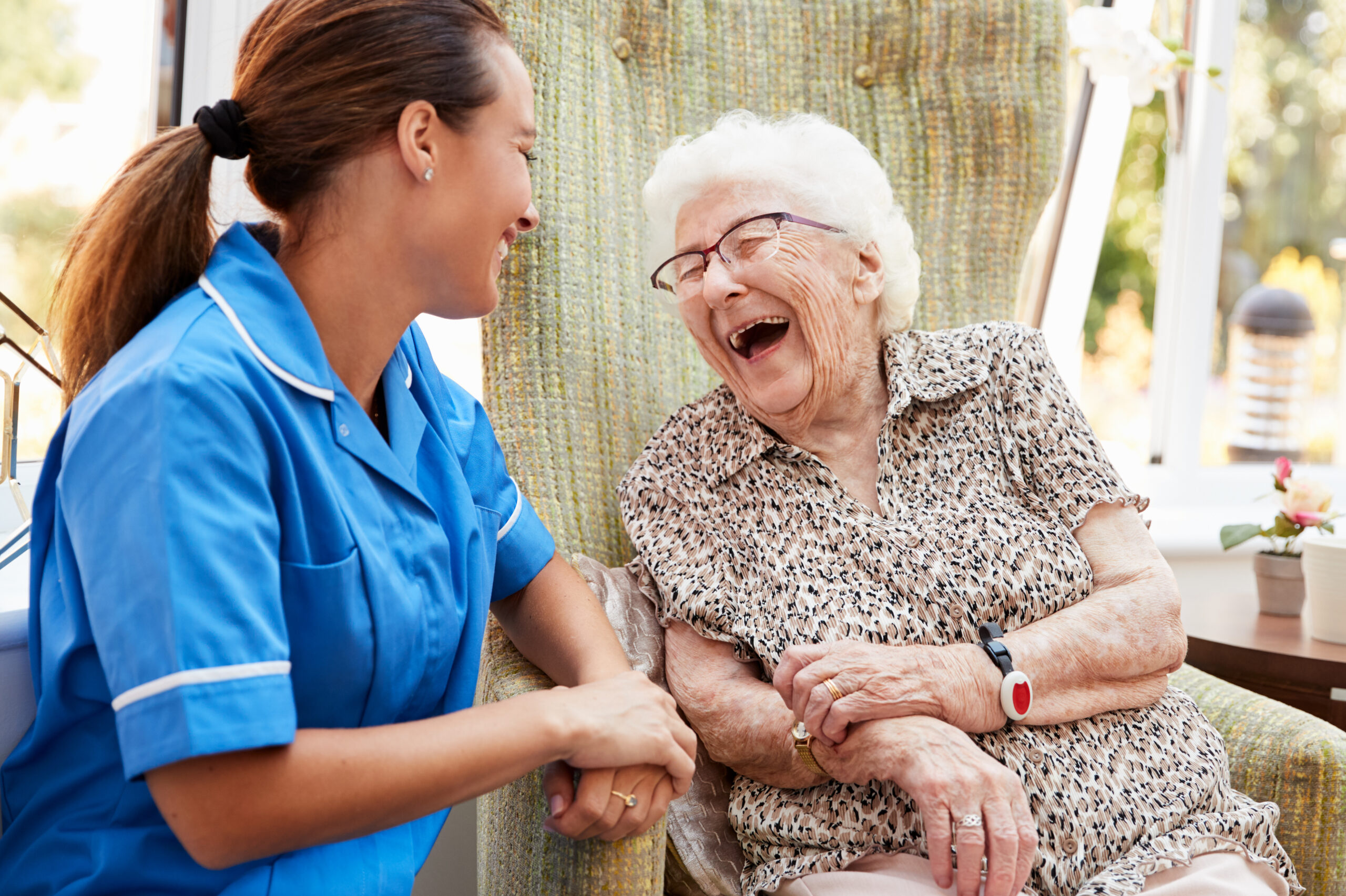An older adult woman laughing with an assisted living team member.