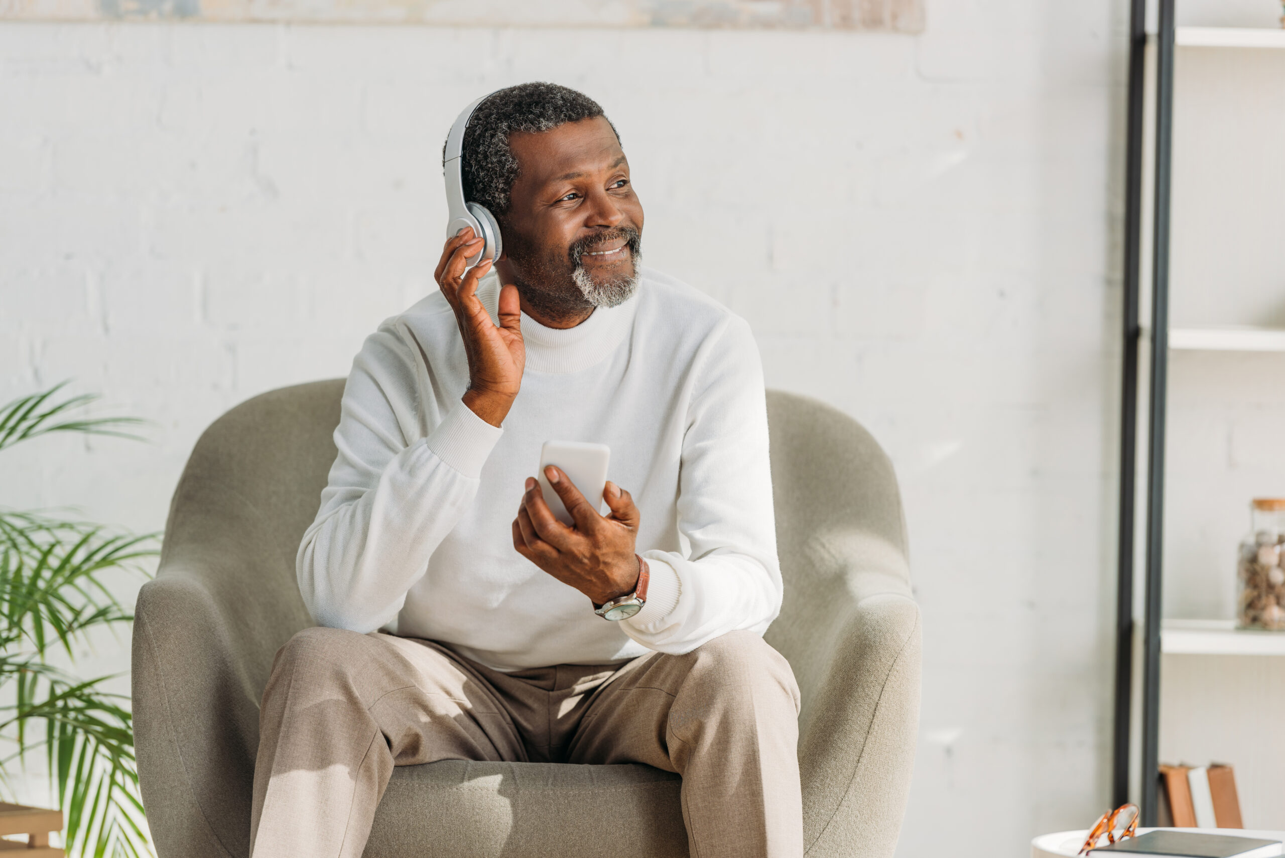 An older adult man smiles as he listens to music with his headphones on.