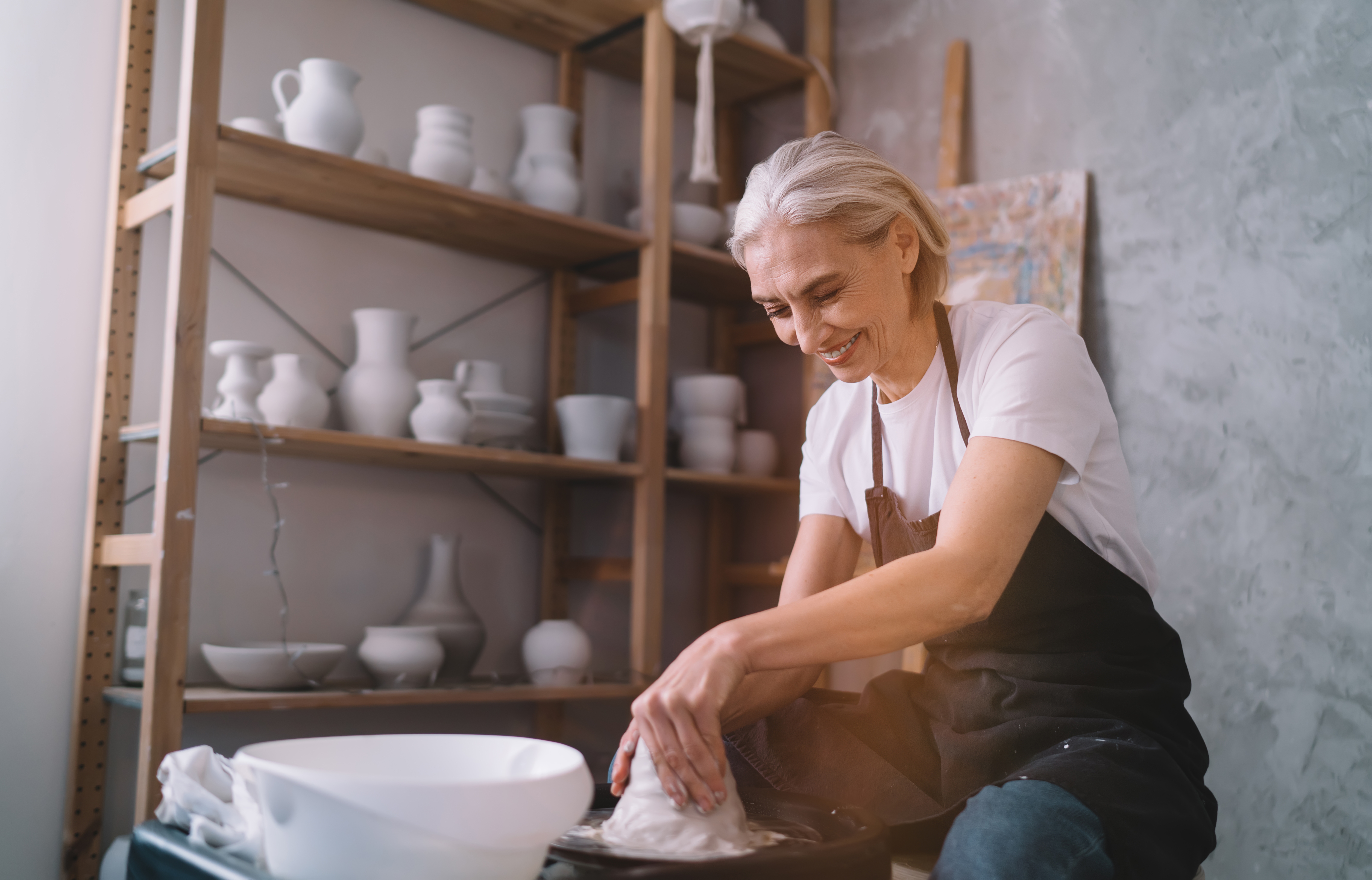 An older adult woman smiling and working with clay.