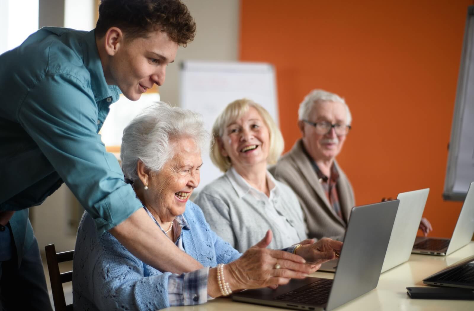 A young staff member in an assisted living community instructs residents on how to use their laptops.