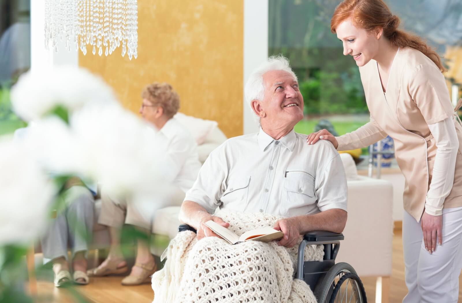A personal care home staff member checks in with an older adult man in a wheelchair.