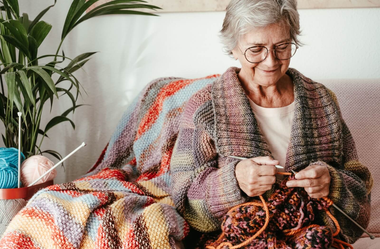 An older adult woman knits a colorful blanket, enjoying her crafting activity.
