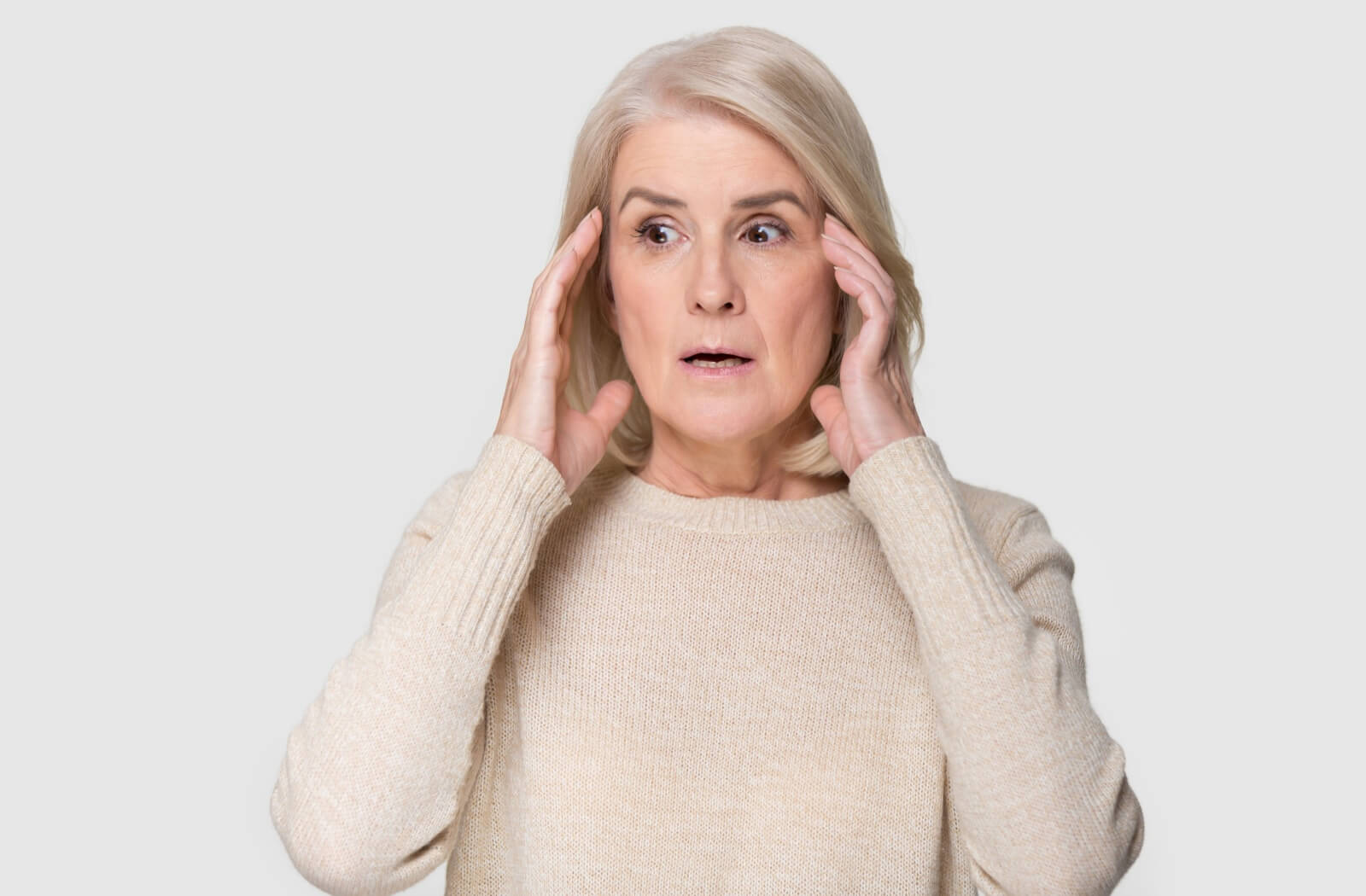 An older adult woman rests her hands on either side of her head with an overwhelmed expression.