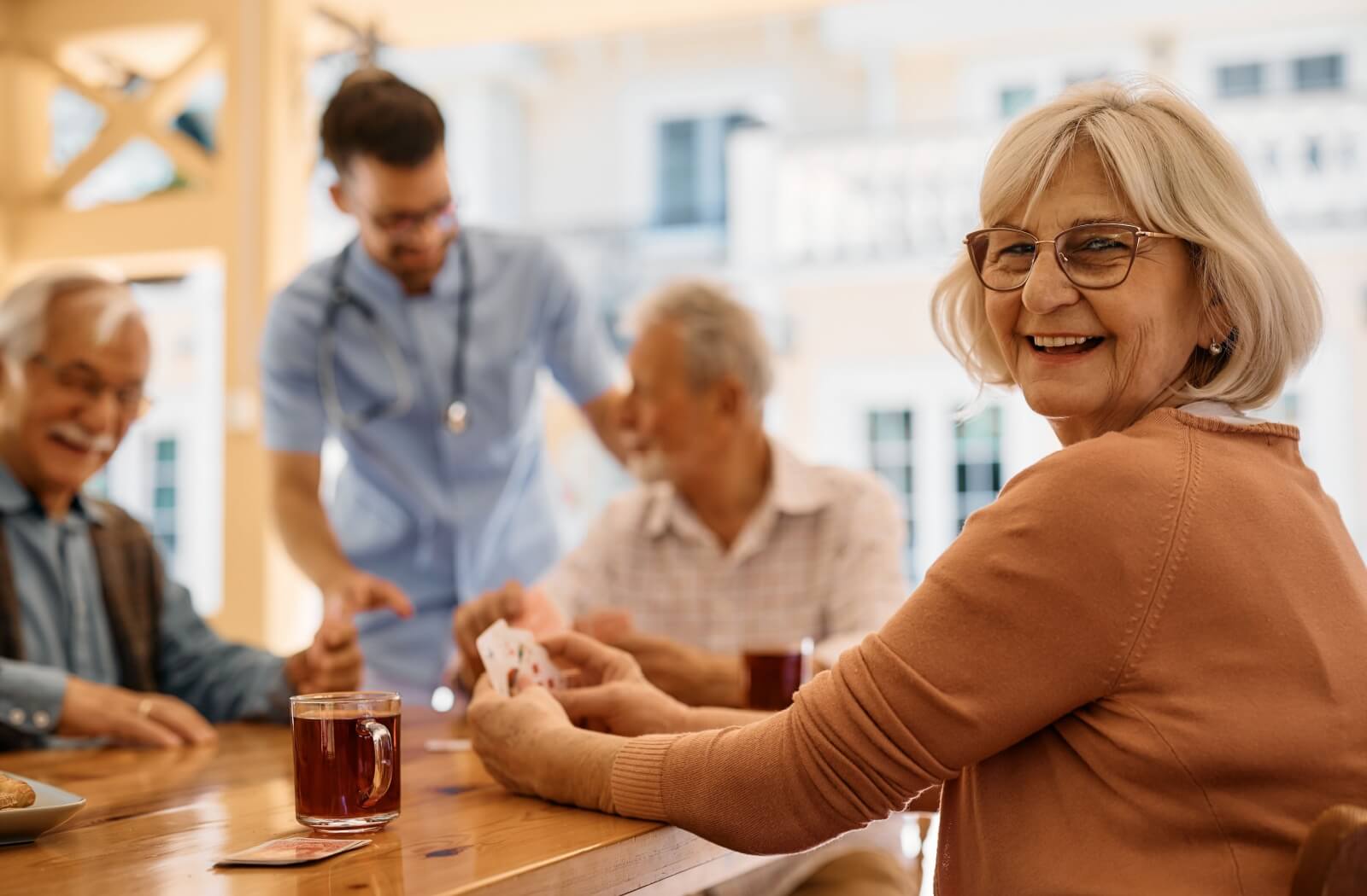 An older adult woman smiling and playing cards with friends on the patio of an assisted living community.