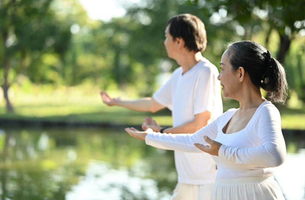 Two older adults perform tai chi exercises outdoors.
