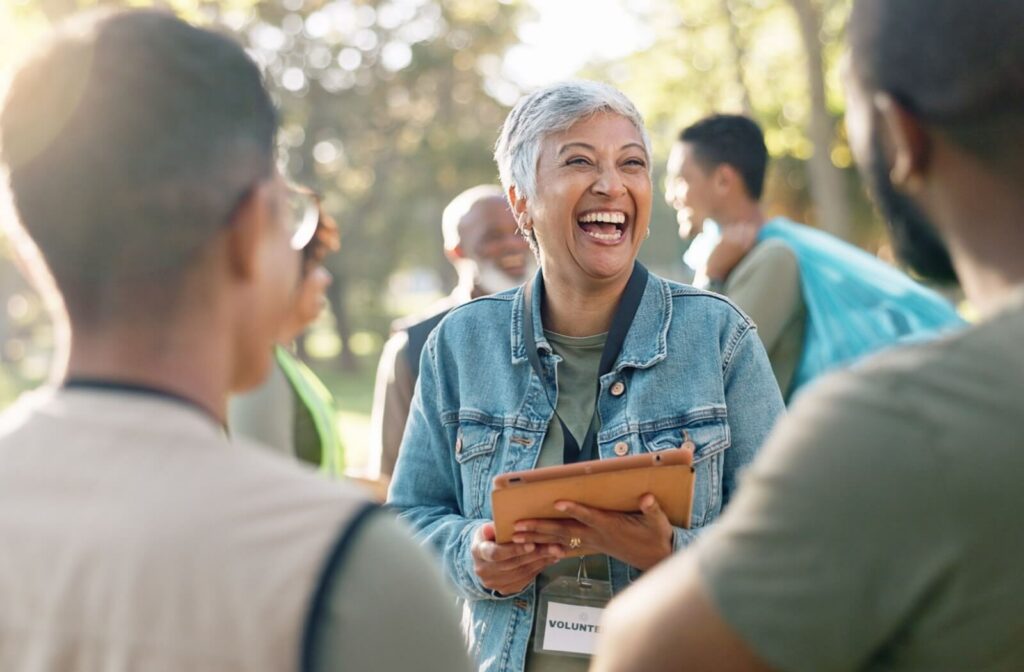 A smiling mature woman volunteers outdoors alongside others.