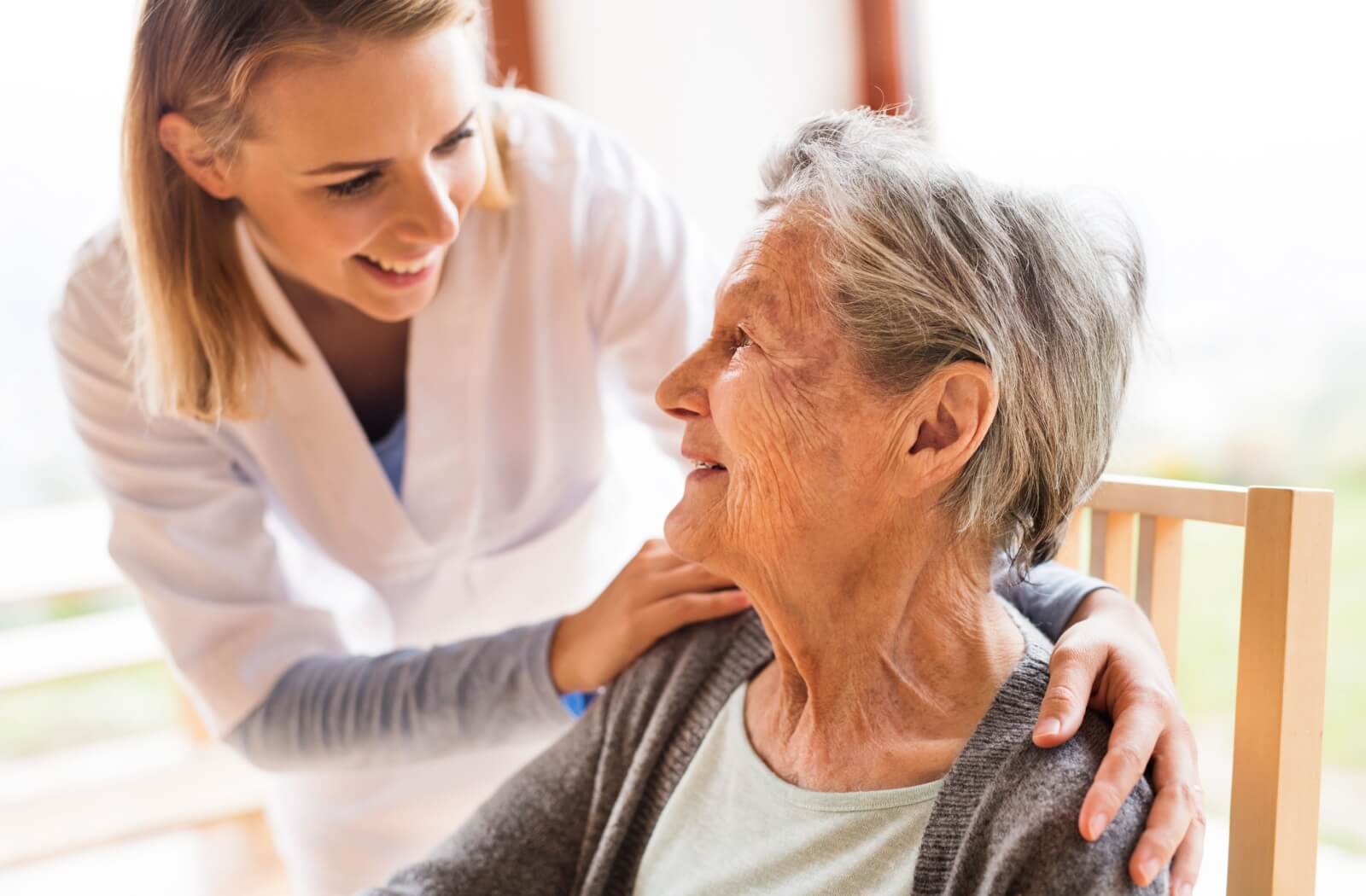 A cheerful nurse checking on a happy older adult woman.