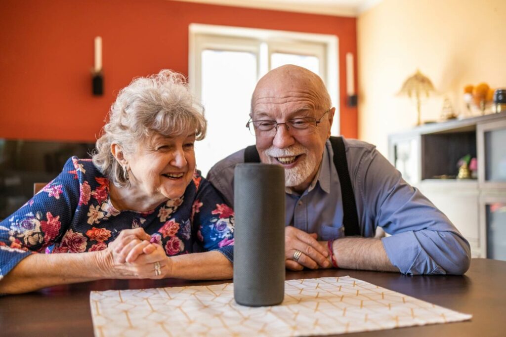 Excited older adult couple marvelling at a virtual assistant device.