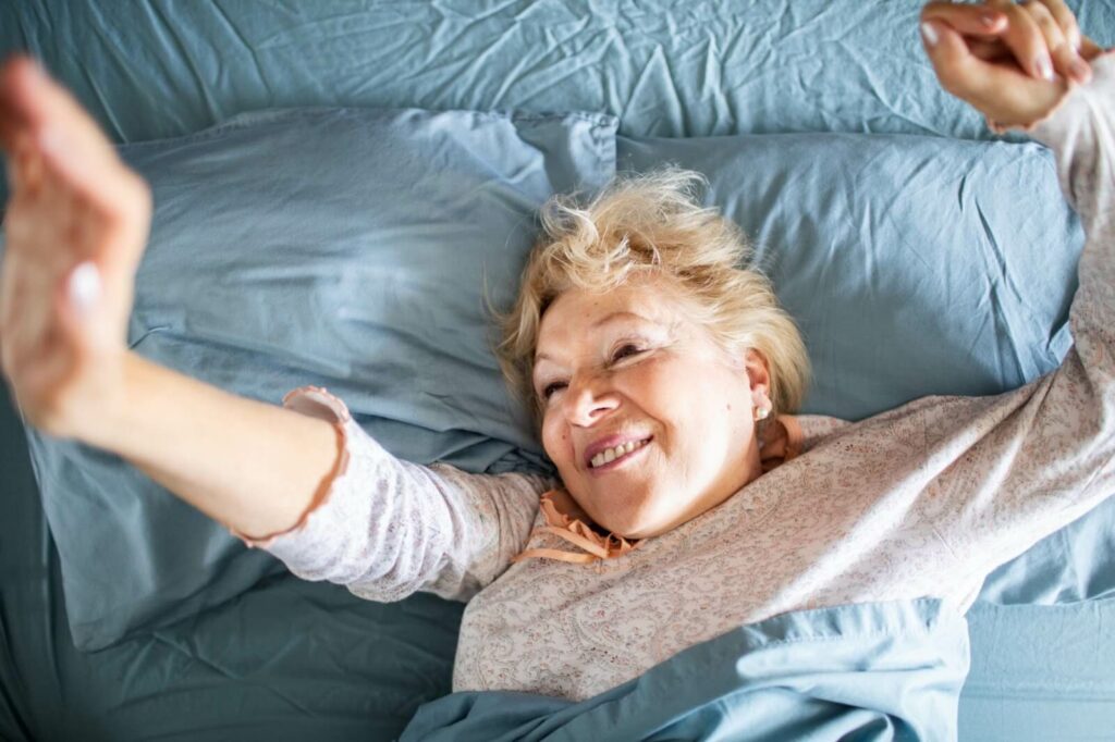 Mature woman stretches her arms and smiles upon waking up in her independent living home.