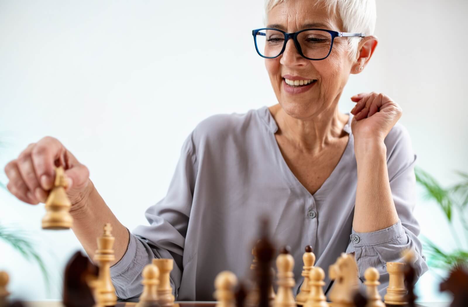 An older adult woman plays chess for mental stimulation.