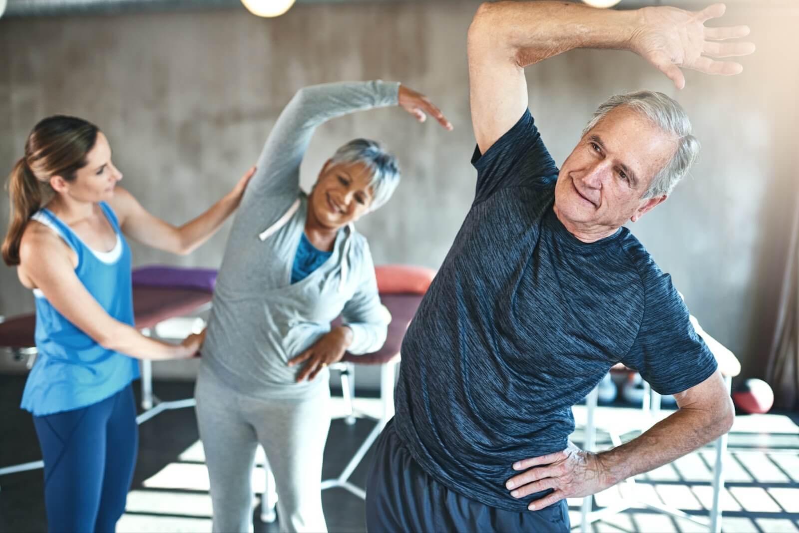 an older adult man and woman stretched under the guidance of an instructor.