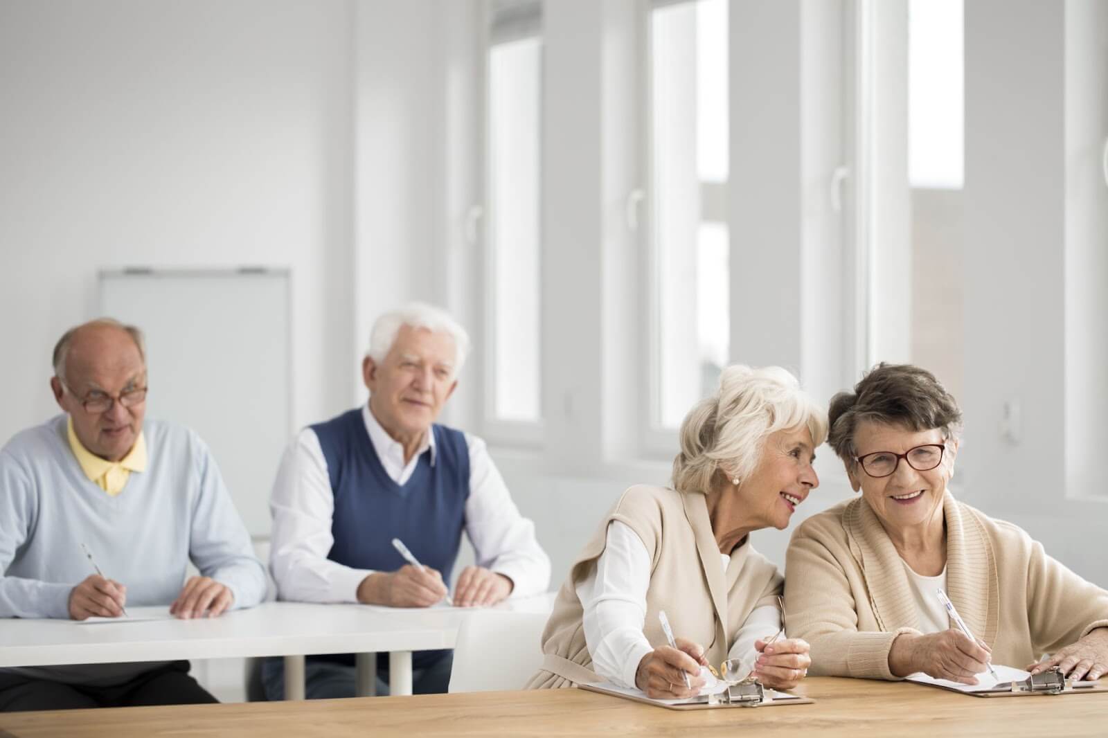 In a learning room at an independent living community, two chatty older adult women sit in front of two older adult men.
