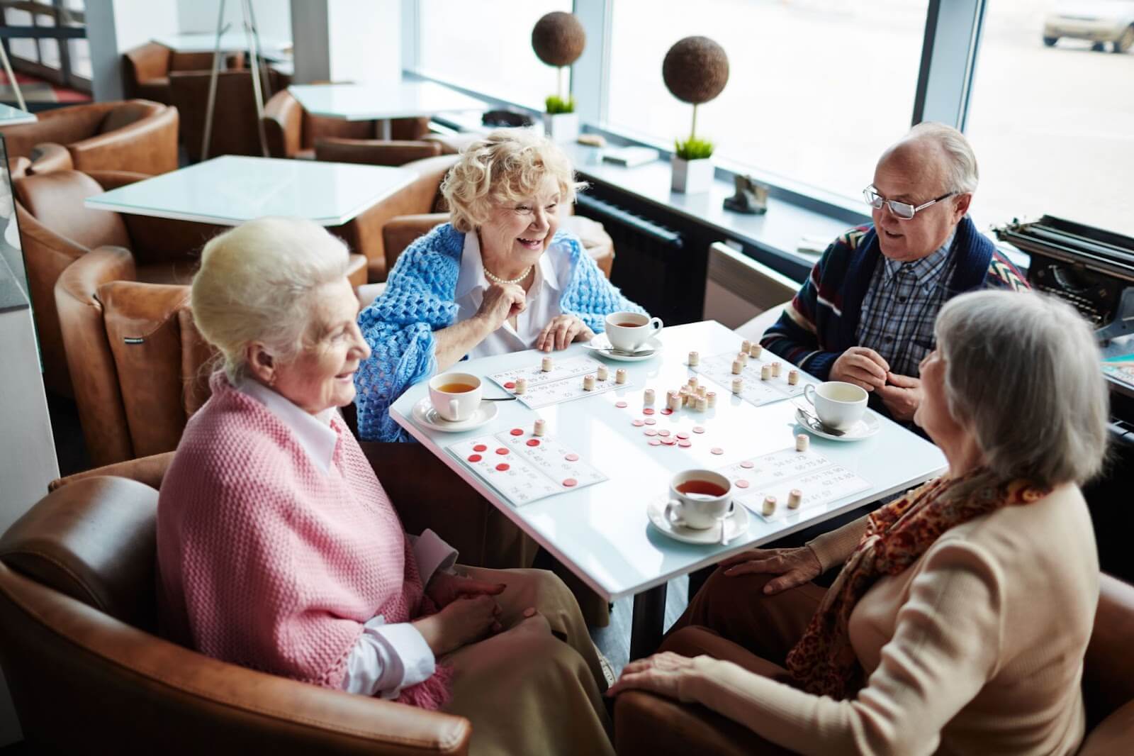 A group of older adults enjoys tea while playing a game of lotto in an assisted living community.