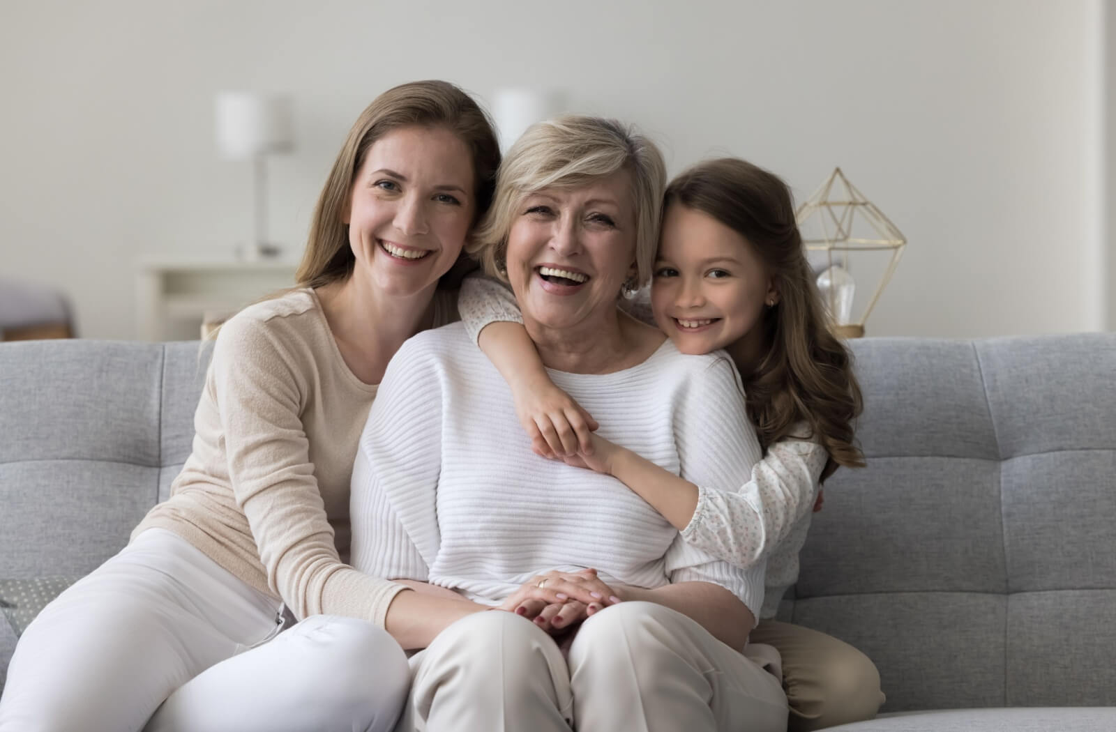 A family of three female generations smiles and hugs each other on the couch.