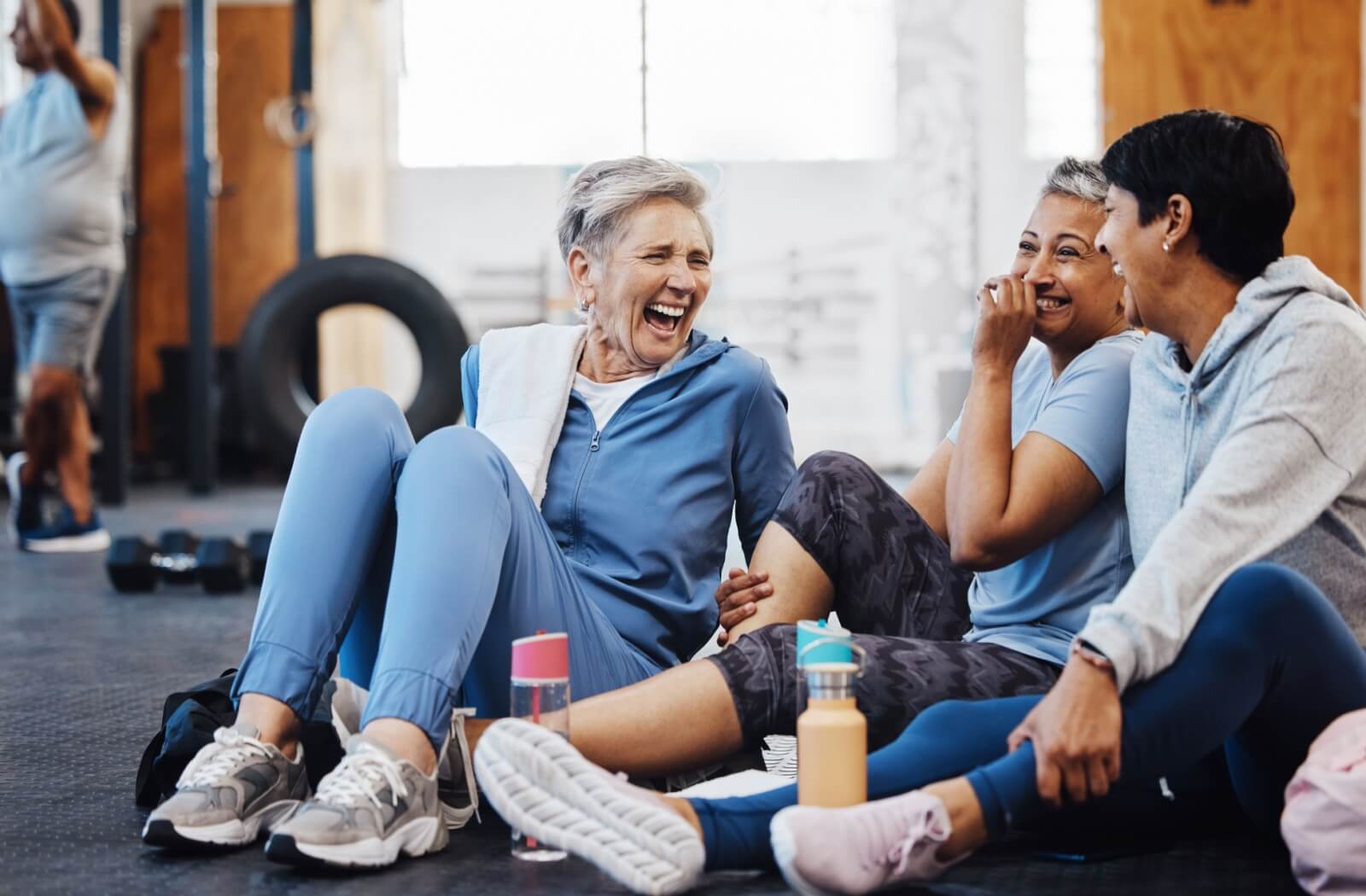 Three mature women laugh together in the gym.