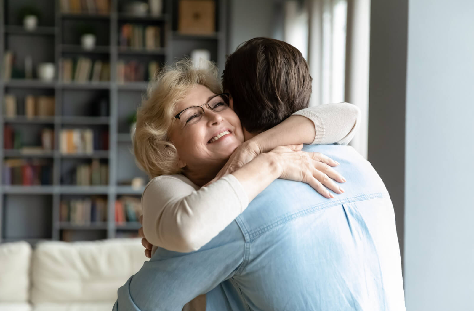 An older adult hugging her son in a brightly lit room.
