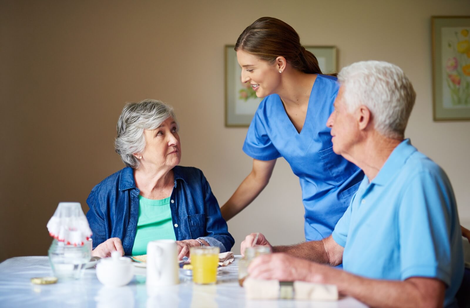 An assisted living nurse supporting older adults during breakfast.