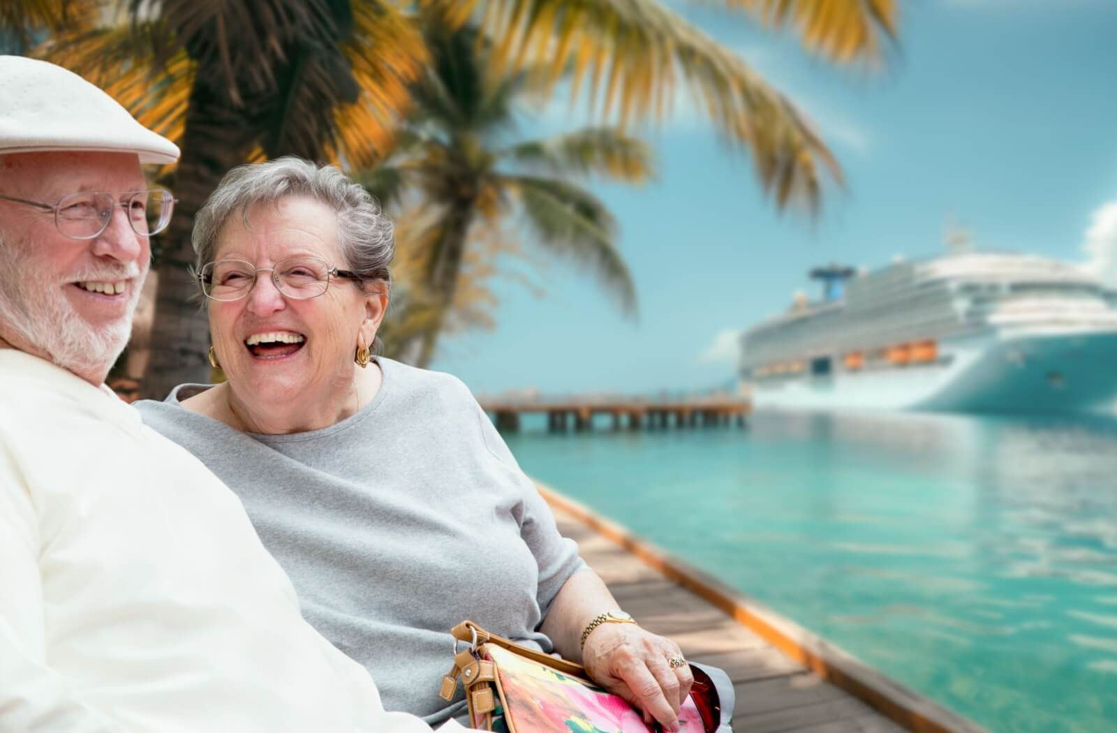 An older adult couple relaxes on the dock, thier cruise vacation is in the background.