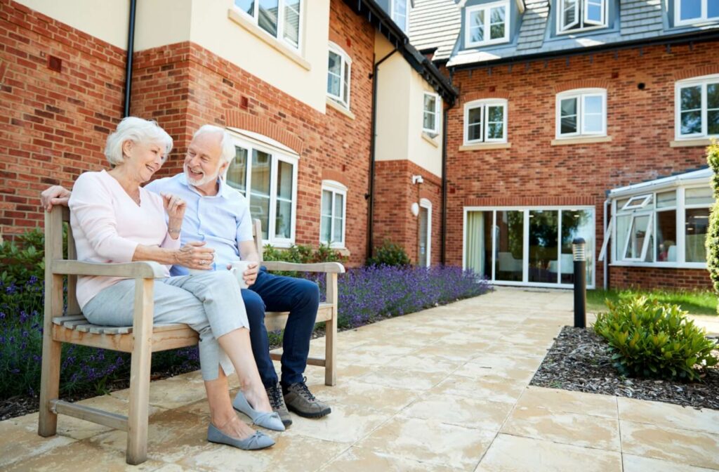 An older adult couple sitting together outside an assisted living community, enjoying a conversation.