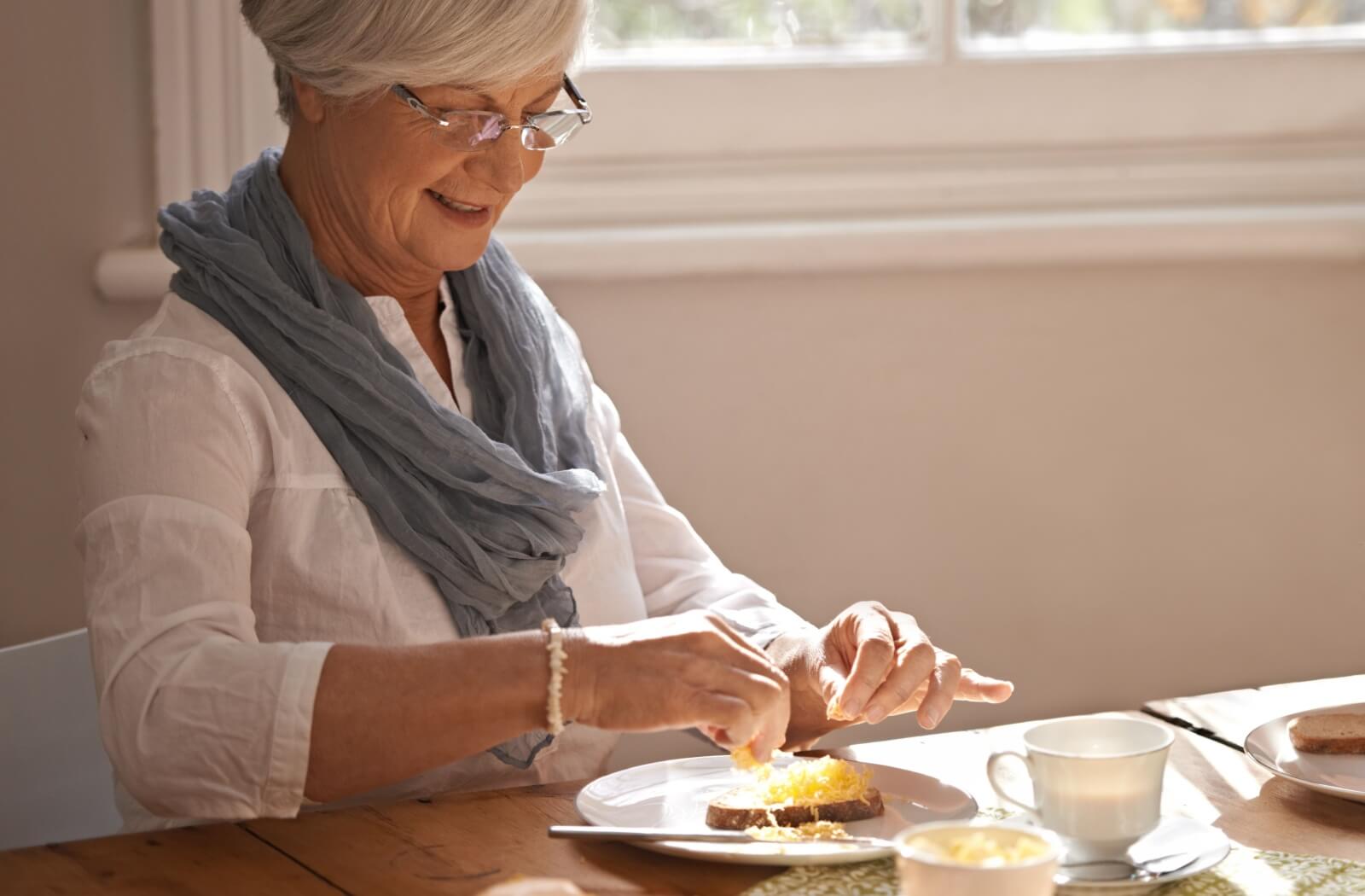 An older adult woman enjoys breakfast in her independent living community.