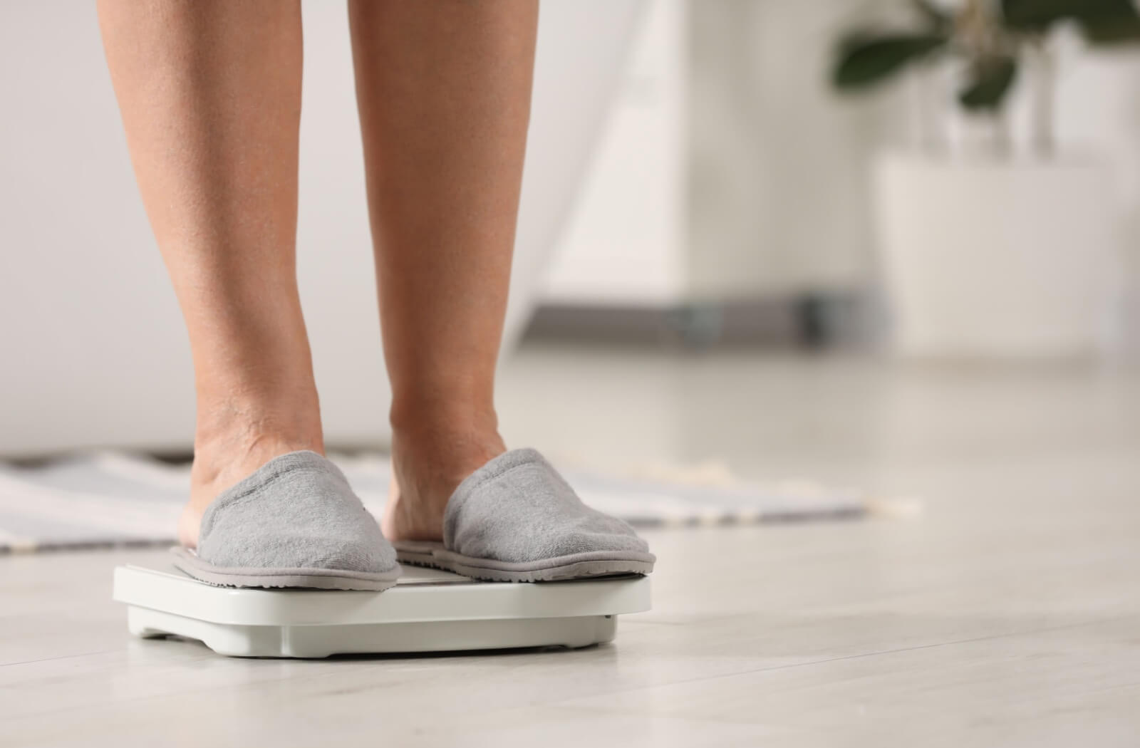 An older adult stands on a weight scale in the bathroom.