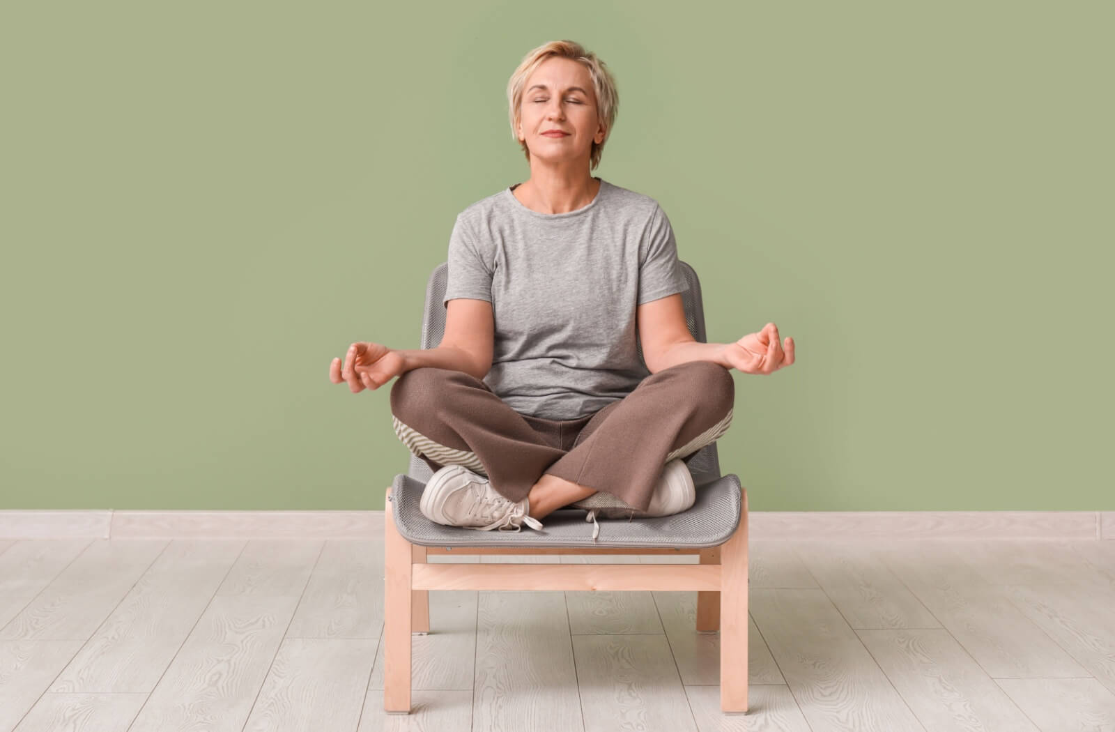 An older adult woman practicing chair yoga exercises at home to improve flexibility and strength.