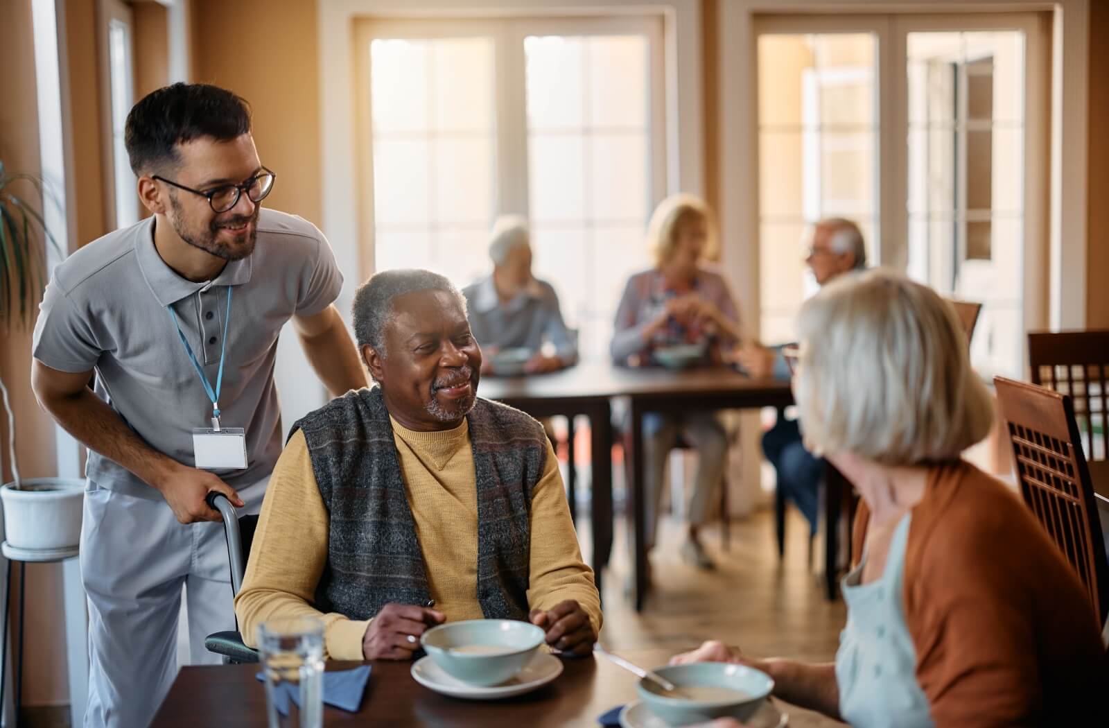 A senior living community caregiver checks in on residents in the dining room.