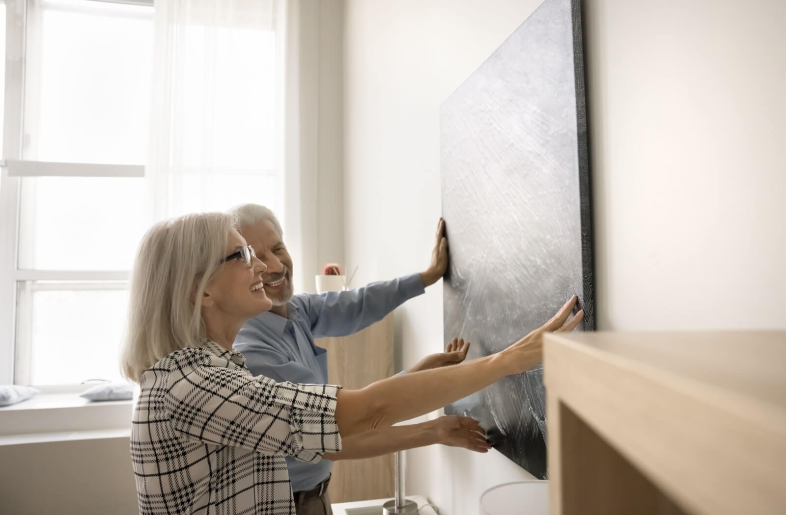 A mature couple hanging a picture in their new assisted living home.