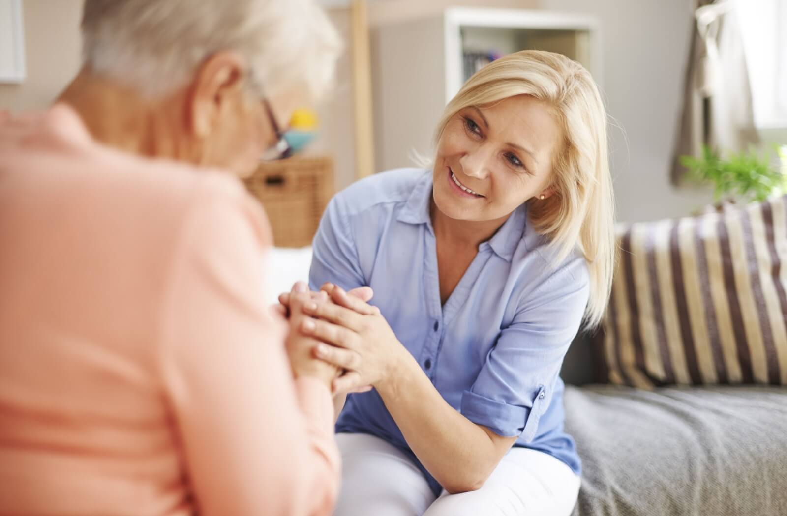 A caregiver holds hands with an older adult woman, both smiling, in an assisted living community.