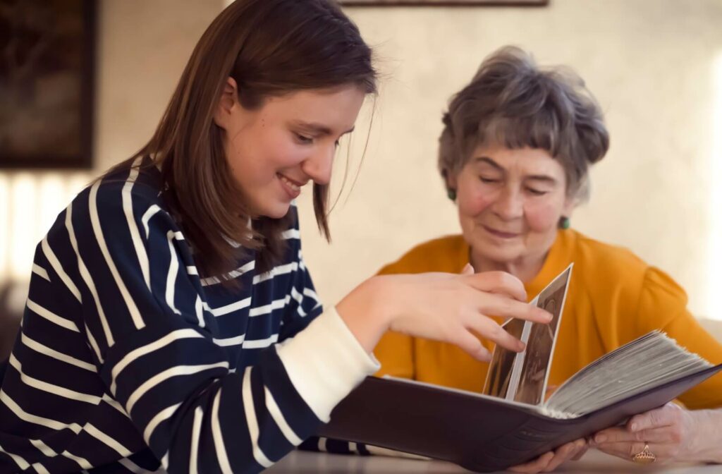 An adult child and their parent look at a photo album together at a table.