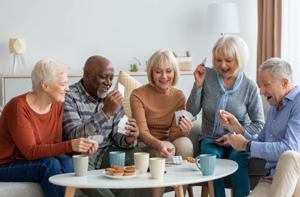 A group of older adults play a card game together while enjoying tea and snacks.
