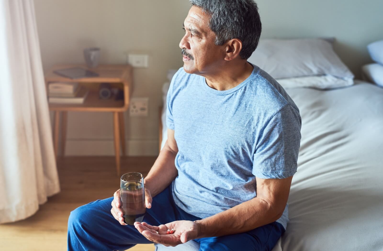 Older adult sitting on the edge of their bed, holding anxiety medication.